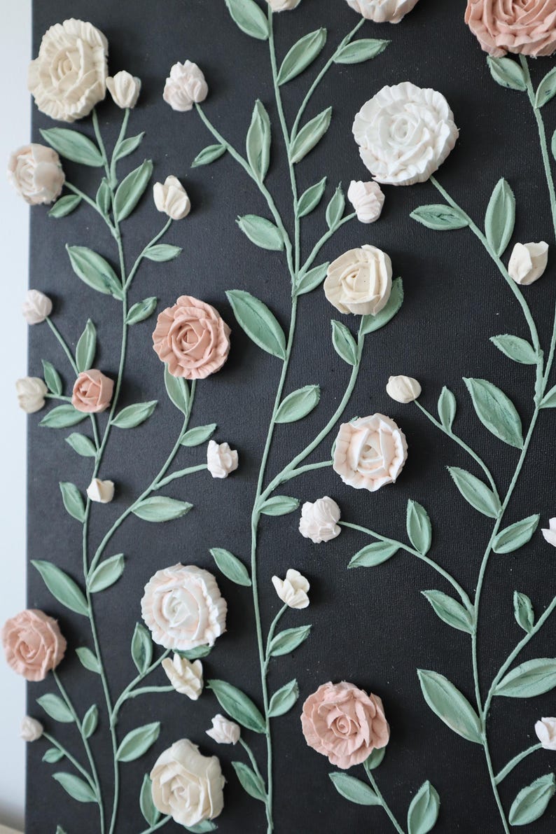 May include: A black canvas with a floral design. The artwork features raised, textured flowers in shades of white and pink, with green stems and leaves. The flowers are arranged in a repeating pattern.