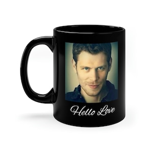 May include: Black ceramic coffee mug with a color photograph of a man with brown hair and a smirk. The text "Hello Love" is printed in white cursive below the photo.
