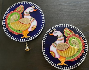 May include: Two round wall decor pieces with a blue background and white peacocks with gold and green accents. Each piece has a white border with a repeating pattern of triangles.
