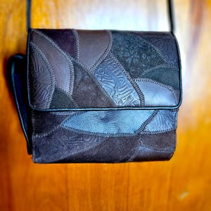 May include: A rectangular shoulder bag constructed from dark brown and black leather patches. The surface features a mix of smooth leather and suede panels, some with embossed floral and swirling patterns, joined together by visible stitching.
