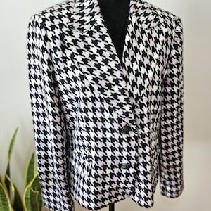 May include: A black and white houndstooth blazer with a double-breasted design. The jacket features a classic notched collar, two rows of black buttons, and a tailored fit. The pattern is a repeating geometric design in black and white.