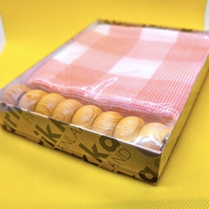 May include: A boxed set of wooden napkin rings and a red and white checkered napkin. The napkin rings are light brown and have a smooth, rounded shape. The napkin is folded and wrapped in clear plastic.