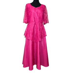 May include: A vibrant hot pink floor-length dress featuring a lace bodice with short sleeves and a peplum waist detail. The skirt is made of a smooth, solid-colored fabric that falls in a straight silhouette from the waist to the hemline.