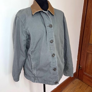 May include: A gray jacket with a brown collar and button closure. The jacket is displayed on a black mannequin and has a classic, casual style. The jacket has a quilted lining and two front pockets.