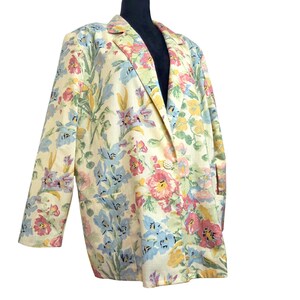 May include: A vintage blazer with a floral pattern in pastel colors. The blazer features a cream-colored base with a vibrant print of pink, blue, yellow, and green flowers. It has a classic lapel, two front pockets, and a button closure.