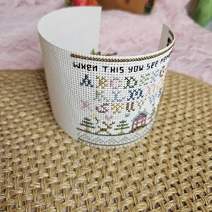Pu&ograve; includere: Tela Aida bianca con un ricamo a punto croce che presenta una casa, alberi e il testo "When this you see may it bring back memories of me".