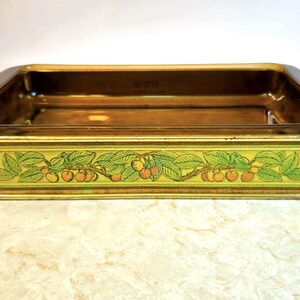 May include: A brown glass baking dish with a gold rim and a floral design featuring green leaves and yellow cherries. The dish is empty.