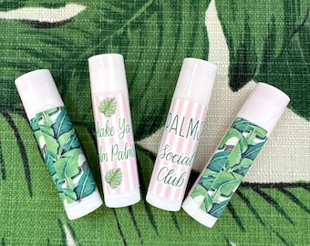 May include: Four pink and white lip balm tubes with tropical leaf designs and text. The text on the tubes reads "Shake Ya Palm", "Palm Social Club", and "Palm Social Club".