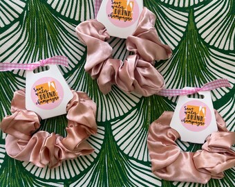 May include: Three pink satin scrunchies with white tags that say "Save water, drink champagne".