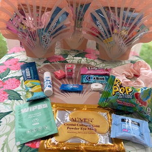 May include: A pink seashell-shaped gift box filled with various small items, including candy, lip balm, face masks, and wipes. The box is surrounded by other items, including a pink and white floral patterned fabric.