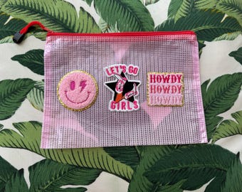 May include: Pink mesh zippered pouch with three embroidered patches. The patches say "Let's Go Girls", "Howdy", and a smiley face with a lightning bolt.