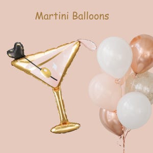 May include: A gold foil martini glass balloon with a pink interior and a black heart charm. The balloon is surrounded by a cluster of white, pink, and gold balloons. The text "Martini Balloons" is written in black at the top of the image.