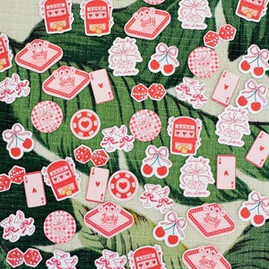 May include: A collection of pink and red stickers with a variety of designs, including cherries, dice, slot machines, martini glasses, and playing cards. The stickers feature the text "Lucky in Love" and "Lucky".