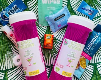 May include: Two pink pill bottles with labels that read "Recovery Prescription" and "Margs and Matrimony". The bottles are surrounded by various items, including lip balm, mints, gum, wipes, and a small packet of electrolyte drink mix.