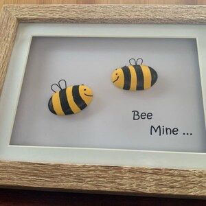 May include: A framed artwork featuring two painted bee designs on stones with the text "Bee Mine..." in black lettering.