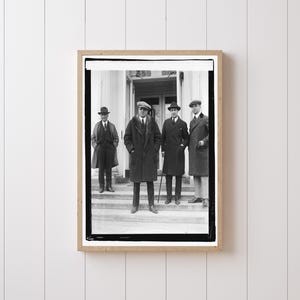 May include: A framed black and white photograph featuring four men in coats and hats standing on steps in front of a building. The men are dressed in formal attire, with one holding a cane. The photograph is in a wooden frame.
