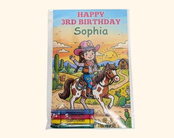 May include: A rectangular coloring sheet in a clear plastic sleeve featuring the text HAPPY 3RD BIRTHDAY Sophia. The illustration shows a person in a cowboy hat riding a brown and white spotted horse in a desert landscape with cacti and a barn.