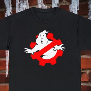 Puede incluir: Camiseta negra con un fantasma blanco que lleva un símbolo rojo de prohibido sobre un engranaje rojo. El fantasma lleva un símbolo rojo de prohibido sobre un engranaje rojo.