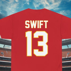 May include: Red t-shirt with the name "SWIFT" and the number "13" printed on the back in white with a yellow outline.