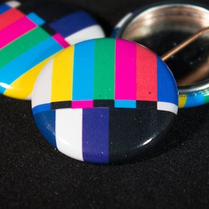 May include: Three round pins with a colorful television test pattern design. The pins are black, white, red, blue, green, and yellow.