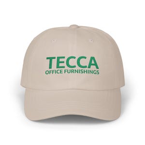 May include: A beige baseball cap with the green text "TECCA OFFICE FURNISHINGS" embroidered on the front. The cap has a curved brim and a fabric strap closure.
