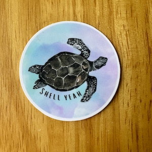 May include: A round sticker with a watercolor background in shades of blue, purple, and pink. A black sea turtle with a white shell is swimming in the water. The text "Shell Yeah" is written below the turtle.