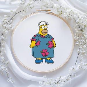 Pode incluir: Bordado em ponto cruz de um personagem de desenho animado em uma camisa havaiana azul com flores rosa, chapéu branco e sapatos azuis. O personagem é amarelo com um nariz bronzeado, em um bastidor de bordado de madeira.