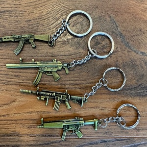May include: Four gold-colored metal gun keychain charms with silver key rings and chains. The guns are different styles of rifles.