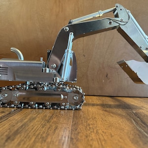 May include: A silver metal toy excavator with a detailed design. The excavator has a long arm with a bucket and tracks.