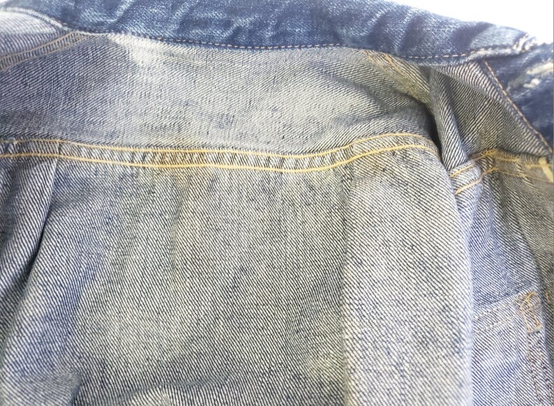 May include: Close-up of the inside of a denim jacket, showing the light blue denim fabric and the yellow stitching along the seams.
