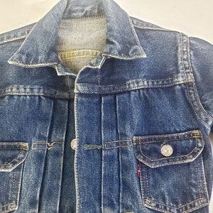 May include: A blue denim jacket with a button closure, two front pockets, and a single pocket on the left chest. The jacket has a faded look and is made of a soft, comfortable material.