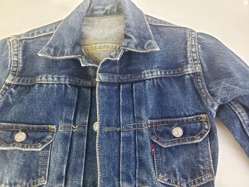 May include: A blue denim jacket with a button closure, two front pockets, and a single pocket on the left chest. The jacket has a faded look and is made of a soft, comfortable material.