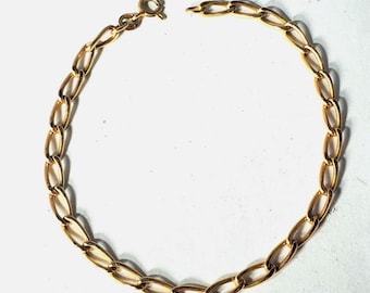 May include: A gold-colored chain bracelet with oval links. The bracelet is shown against a white background. The clasp is open, revealing the end of the chain. The bracelet is a delicate piece of jewelry.