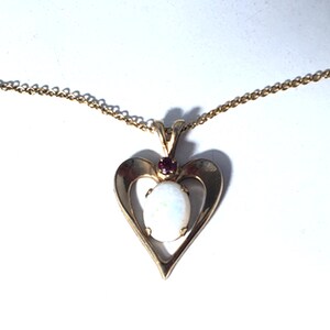 May include: A gold heart-shaped pendant necklace with a white opal stone and a small red ruby accent.