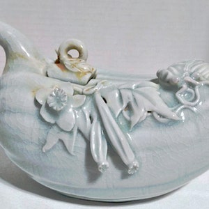 Könnte beinhalten: Eine weiße Teekanne aus Keramik mit hellblauer Glasur. Die Teekanne ist in Form einer Kalebasse geformt und hat einen Deckel mit einem Vogelmotiv. Die Teekanne ist mit floralen und Blattmotiven verziert.