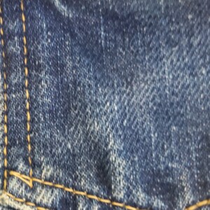 May include: Close-up of a blue denim fabric with a red Levi's label and a gold paperclip attached to it.