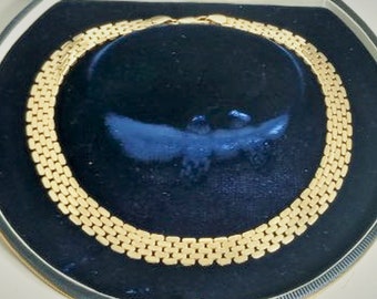 Könnte beinhalten: Eine goldene Kettenkette mit einem Gliederdesign. Die Kette wird auf einem schwarzen Samt-Hintergrund präsentiert.