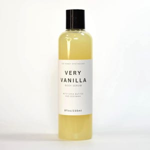 May include: A clear bottle of Very Vanilla Body Serum with a black cap. The label reads "Very Vanilla Body Serum" with the ingredients "with Shea Butter and Beeswax". The bottle contains 8 fl oz / 235ml of serum.
