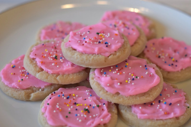 May include: A plate of pink frosted sugar cookies with colorful sprinkles. The cookies are stacked on top of each other.