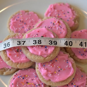 May include: A plate of pink frosted sugar cookies with colorful sprinkles, measured with a tape measure. The tape measure reads 34 to 42 inches.