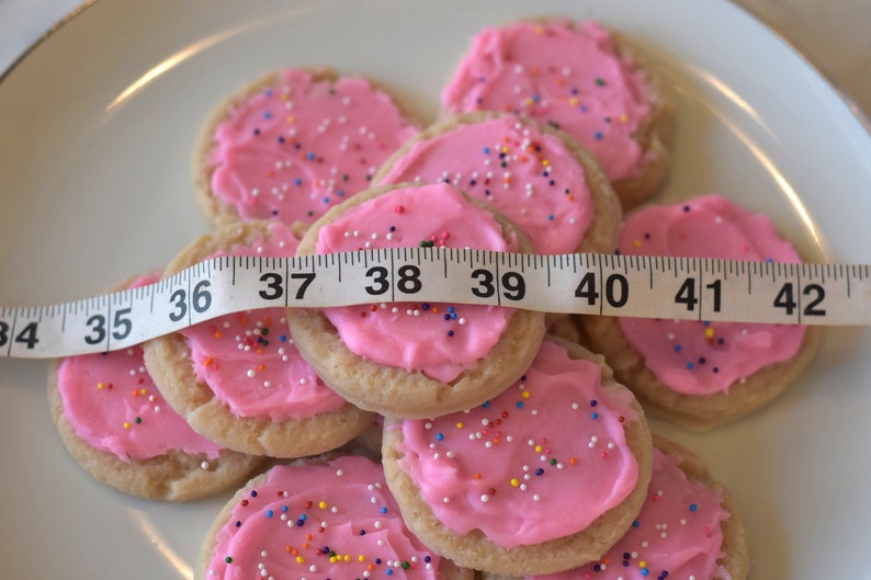May include: A plate of pink frosted sugar cookies with colorful sprinkles, measured with a tape measure. The tape measure reads 34 to 42 inches.