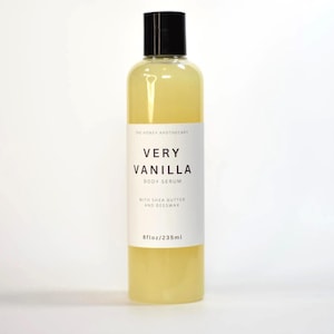 May include: A clear bottle of Very Vanilla Body Serum from The Honey Apothecary. The bottle has a black cap and a white label with the product name and details. The bottle contains 8 fl oz / 235 ml of a yellow liquid.