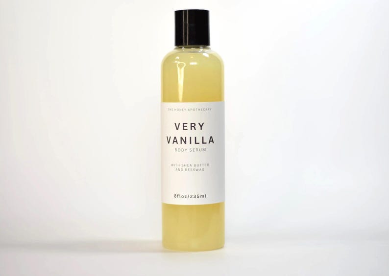 May include: A clear bottle of Very Vanilla Body Serum from The Honey Apothecary. The bottle has a black cap and a white label with the product name and details. The bottle contains 8 fl oz / 235 ml of a yellow liquid.