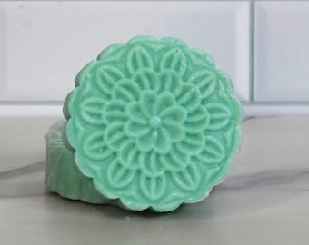 May include: A round, light green soap bar with a decorative floral design.