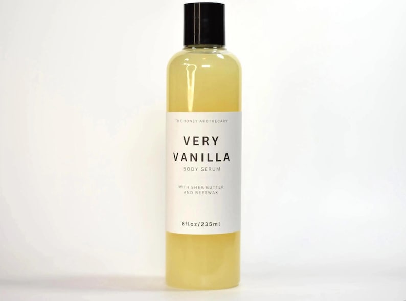 May include: A clear bottle of Very Vanilla Body Serum with a black cap. The label reads "Very Vanilla Body Serum" with "With Shea Butter and Beeswax" below. The bottle contains 8 fl oz / 235ml of serum.