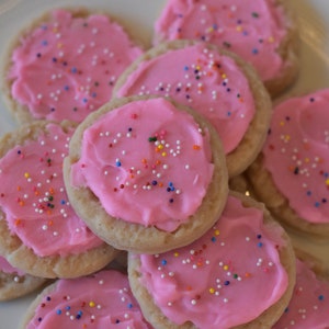 May include: A plate of pink frosted sugar cookies with colorful sprinkles. The cookies are arranged in a circle with the frosting facing up.
