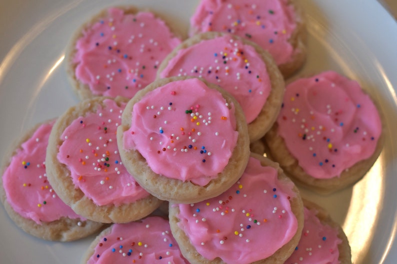 May include: A plate of pink frosted sugar cookies with colorful sprinkles. The cookies are arranged in a circle with the frosting facing up.