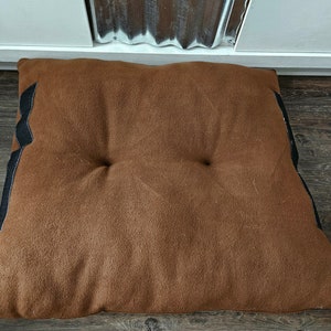 May include: A brown, rectangular floor cushion with black trim. The cushion has two buttons on the top.