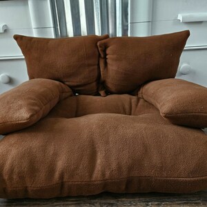 May include: A brown, plush, floor cushion with four attached pillows. The cushion is designed to be used as a comfortable seating option.
