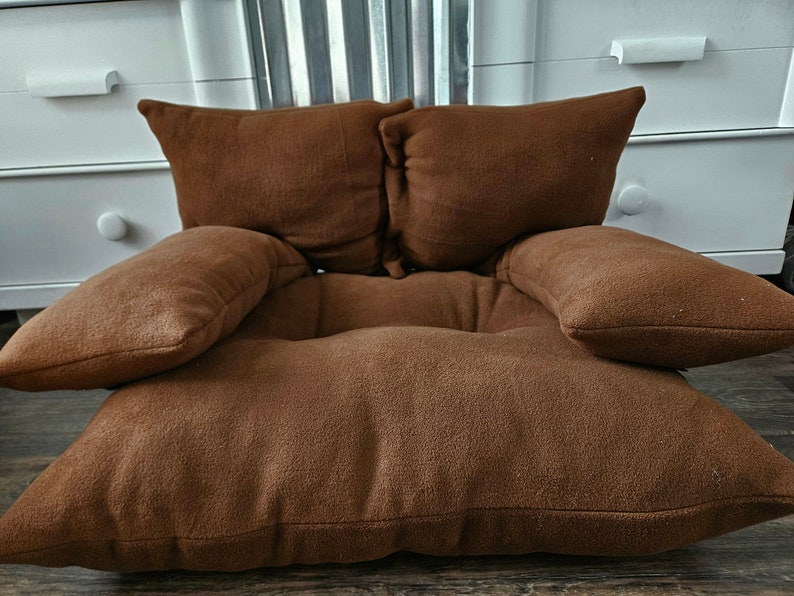 May include: A brown, plush, floor cushion with four attached pillows. The cushion is designed to be used as a comfortable seating option.